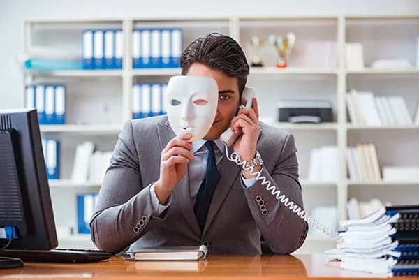 homme en costume tenant un masque devant son visage au téléphone dans un bureau