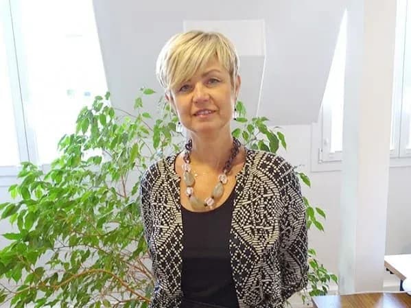 femme souriante avec un collier devant une plante verte dans un bureau lumineux