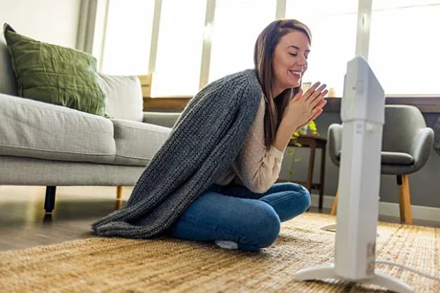 femme assise par terre avec une couverture devant un chauffage d'appoint en hiver