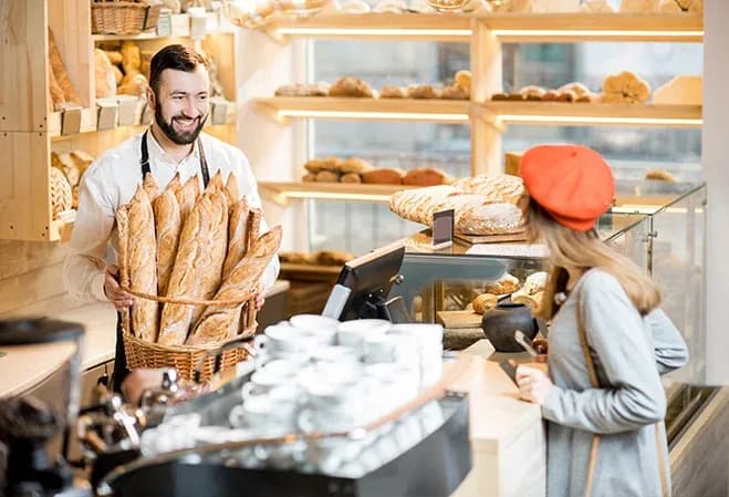 un boulanger souriant sert une cliente dans une boulangerie avec des pains en arrière-plan