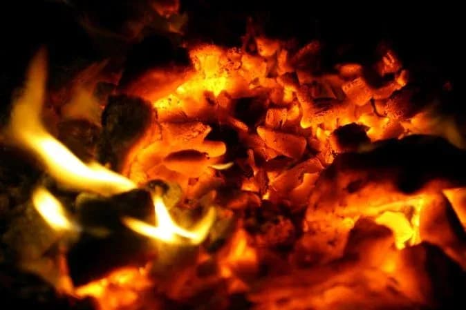 flammes et braises éclairant un tas de cendres dans l'obscurité