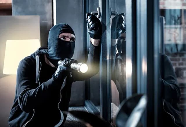 homme masqué avec une lampe de poche tentant d'ouvrir une fenêtre dans un intérieur sombre