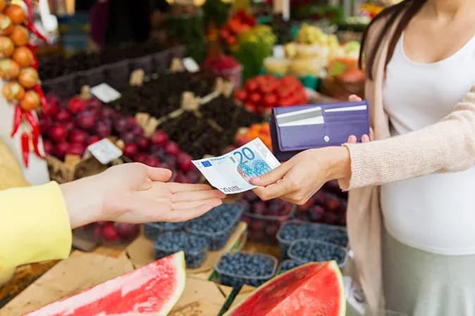 billet de 20 euros échangé entre un vendeur et un client sur un marché coloré
