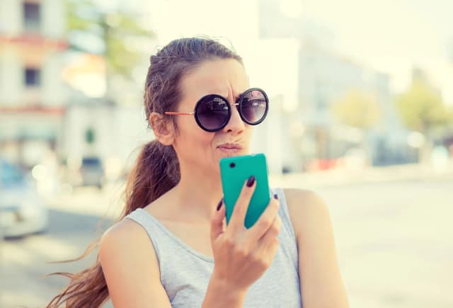 femme avec des lunettes de soleil regardant son téléphone avec une expression perplexe