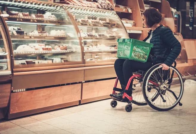 femme en fauteuil roulant regardant des pâtisseries dans une vitrine de magasin