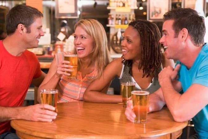 Quatre amis rient autour d'une table au bar en tenant des verres de bière