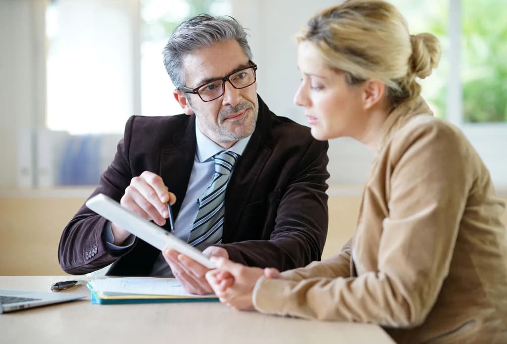 discussion entre un homme en costume et une femme sur un document à une table en intérieur