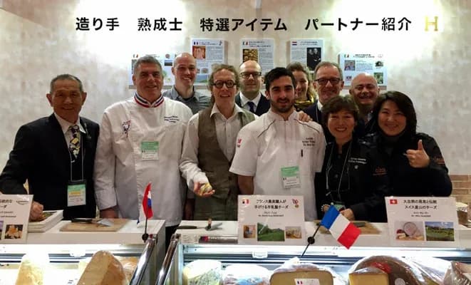 groupe de professionnels de la gastronomie posant devant un stand de fromage