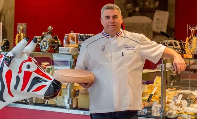 fromager tenant un plateau avec un fromage devant un comptoir rempli de produits laitiers