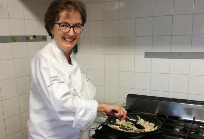 femme souriante en blouse de chef cuisinant dans une cuisine moderne