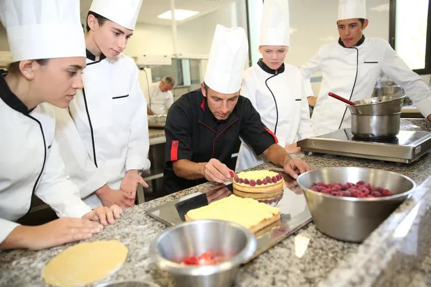 apprentis pâtissiers observant un chef décorer un gâteau avec des fruits rouges en cuisine