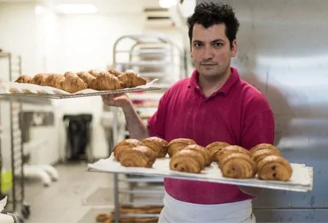 boulanger portant des plateaux de viennoiseries dans une boulangerie moderne
