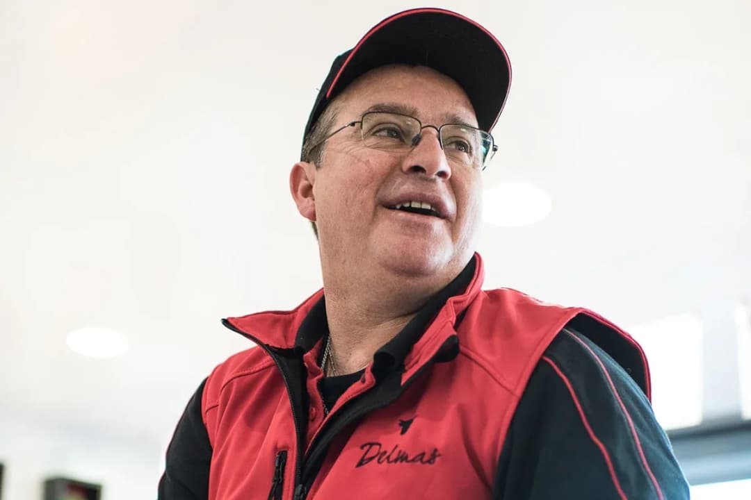 Homme souriant portant une veste rouge et une casquette dans un environnement lumineux
