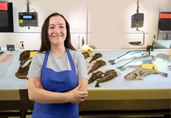 femme souriante en tablier bleu devant un étal de poissons frais dans un marché