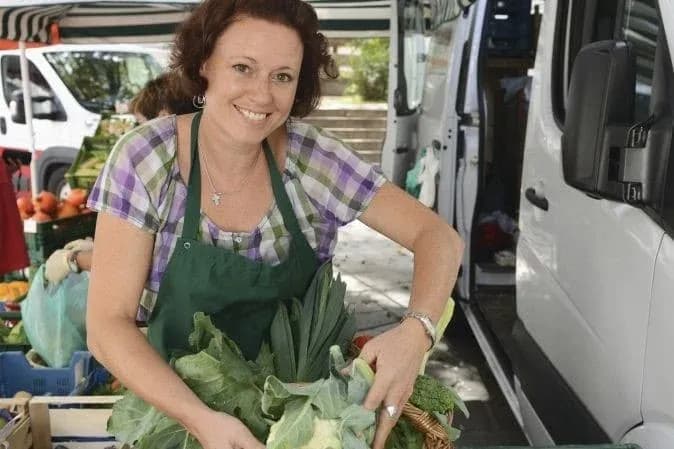 femme souriante tenant des légumes au marché avec des étals en arrière-plan