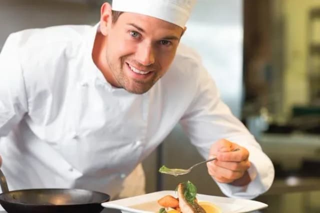 chef souriant préparant un plat avec du poisson et des légumes dans une cuisine professionnelle