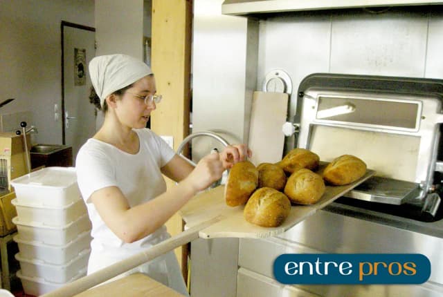 femme en train de sortir des pains du four avec une pelle à pain dans une boulangerie