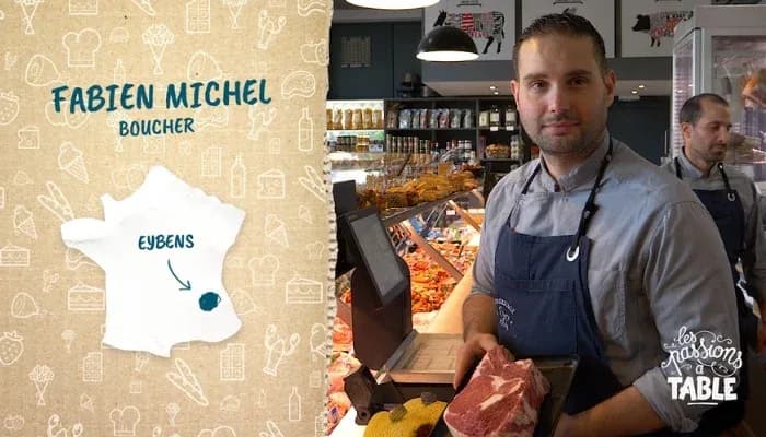 boucher tenant un morceau de viande dans une boucherie avec un autre boucher en arrière-plan