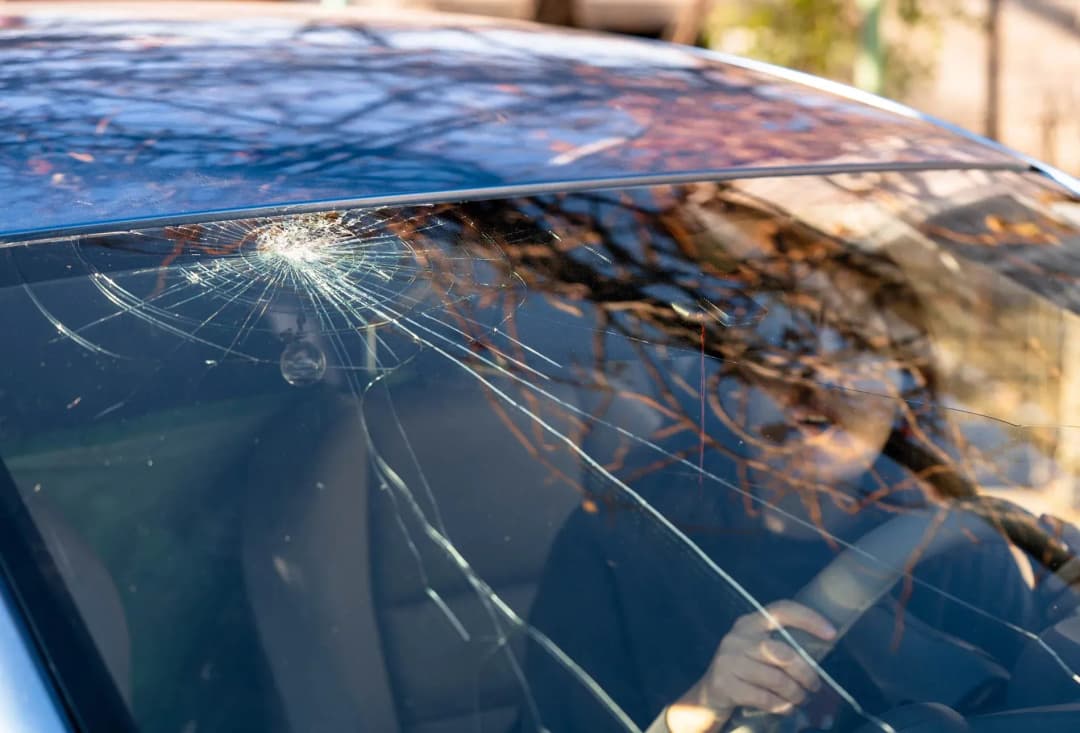 pare-brise fissuré avec des rayures visibles et une personne au volant de la voiture