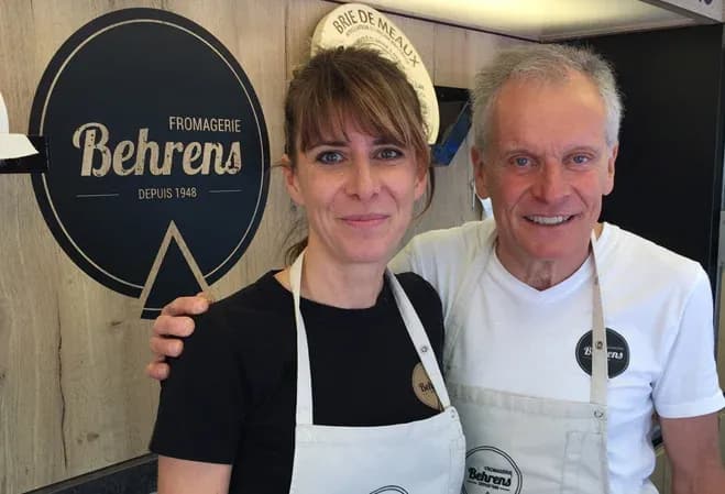 deux personnes souriantes devant un comptoir de fromagerie avec un logo en arrière-plan