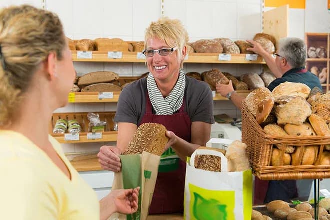 vendeuse remet un pain complet emballé à une cliente au comptoir de la boulangerie
