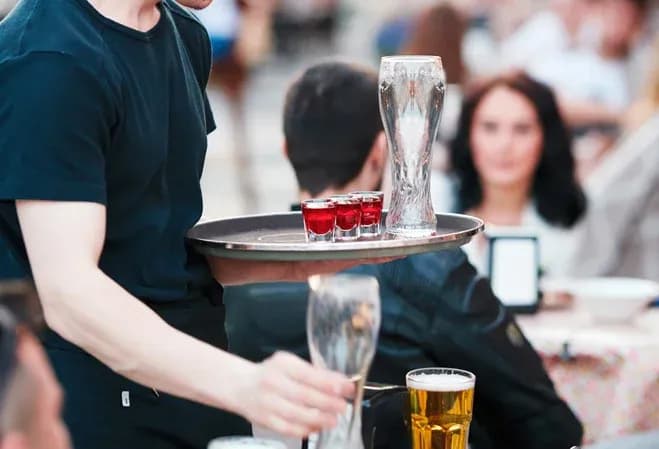 serveur portant un plateau avec des verres à shot et des pintes dans un café animé