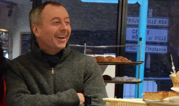 Homme souriant assis près d'une vitrine avec des pâtisseries en arrière-plan