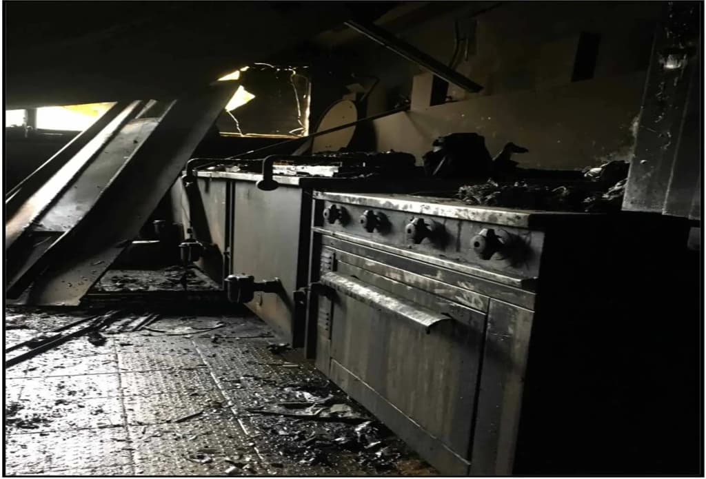 cuisine endommagée par un incendie avec des appareils noircis et des débris au sol