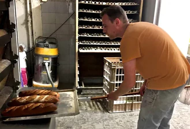 Boulanger en train de sortir des baguettes du four dans une boulangerie artisanale
