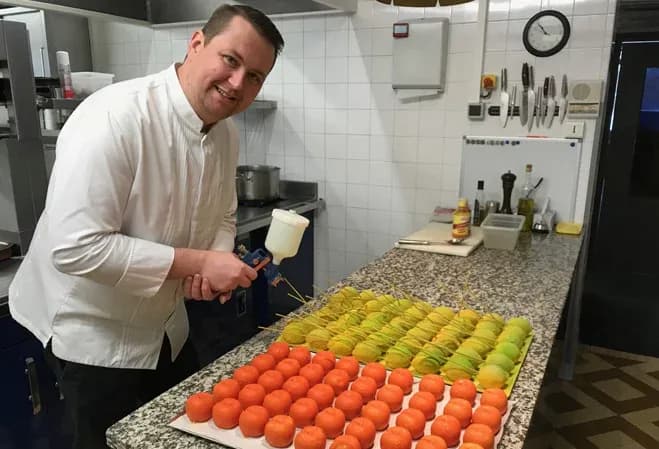 Chef souriant préparant des desserts colorés dans une cuisine professionnelle moderne