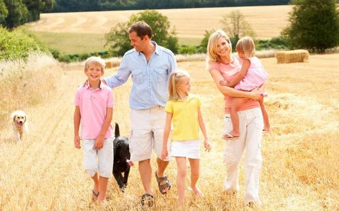 parents et trois enfants marchant avec deux chiens dans un champ moissonné