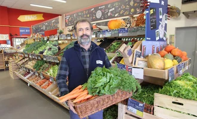 Homme souriant tenant un panier de légumes frais dans un magasin de produits bio