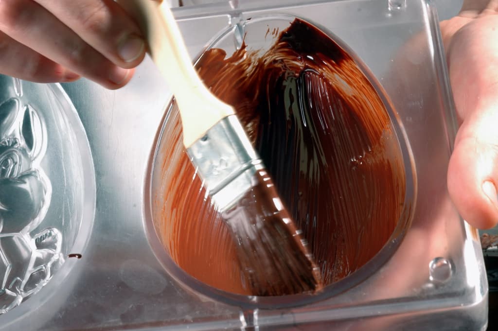 application de chocolat fondu dans un moule en forme d'œuf avec un pinceau