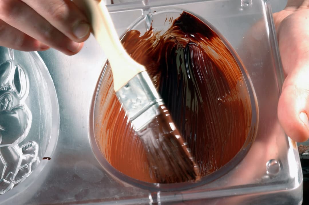 application de chocolat fondu dans un moule en forme d'œuf avec un pinceau
