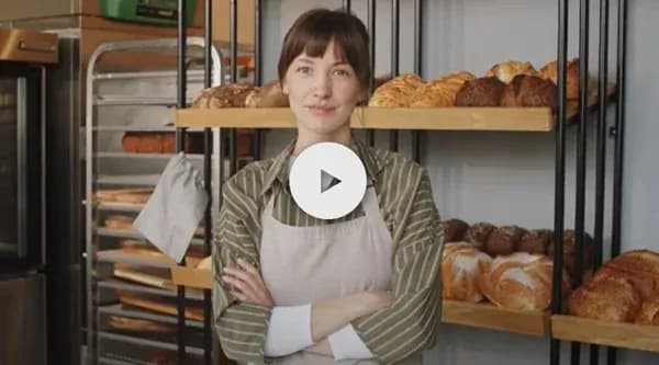 femme souriante dans une boulangerie avec des pains et viennoiseries en arrière-plan