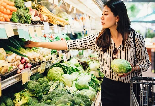 femme choisissant des légumes frais dans un supermarché avec un caddie à côté d'elle
