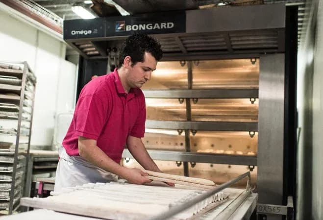 un boulanger en train de préparer des baguettes devant un four professionnel