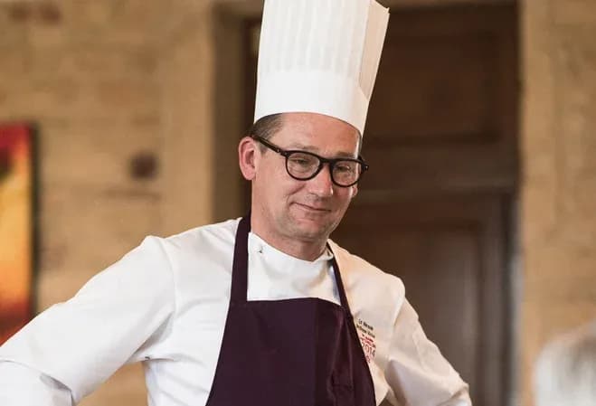 chef souriant portant une toque et un tablier dans un cadre chaleureux de restaurant