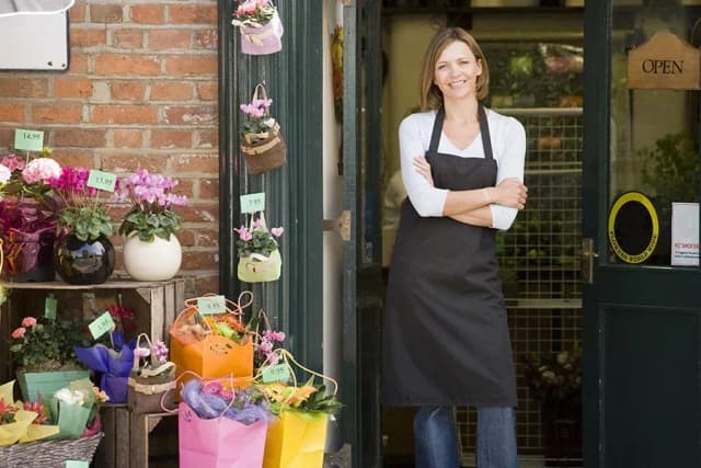 fleuriste souriante devant sa boutique avec des fleurs colorées exposées à l'extérieur