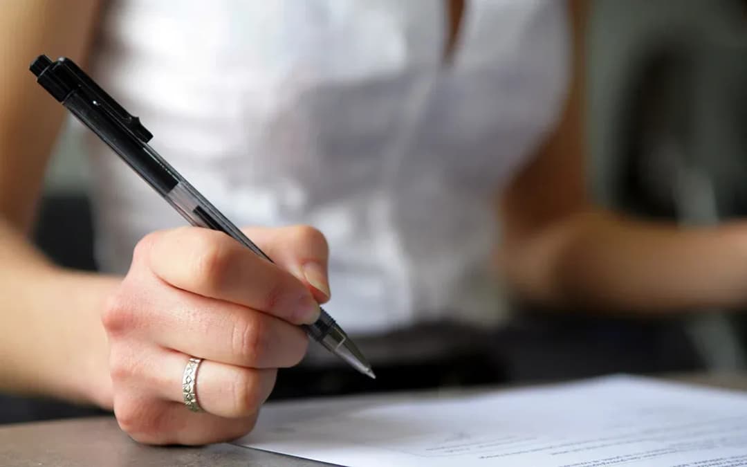 main tenant un stylo et écrivant sur un document posé sur une table