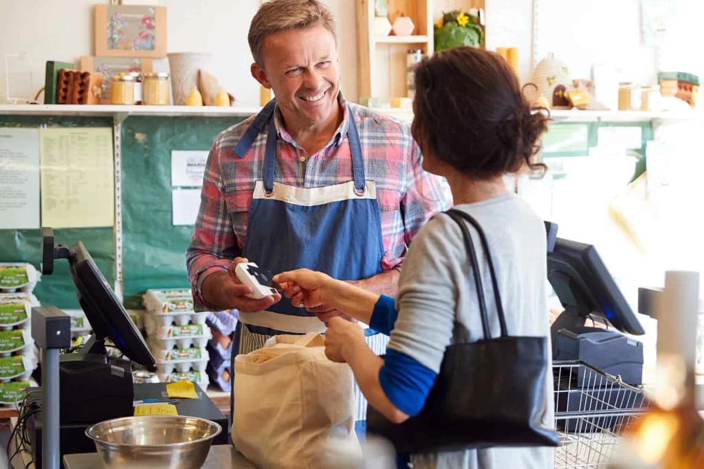 Homme souriant servant une cliente dans un magasin rural avec des produits en arrière-plan