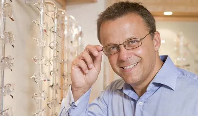Homme souriant ajustant des lunettes devant un présentoir d'optique