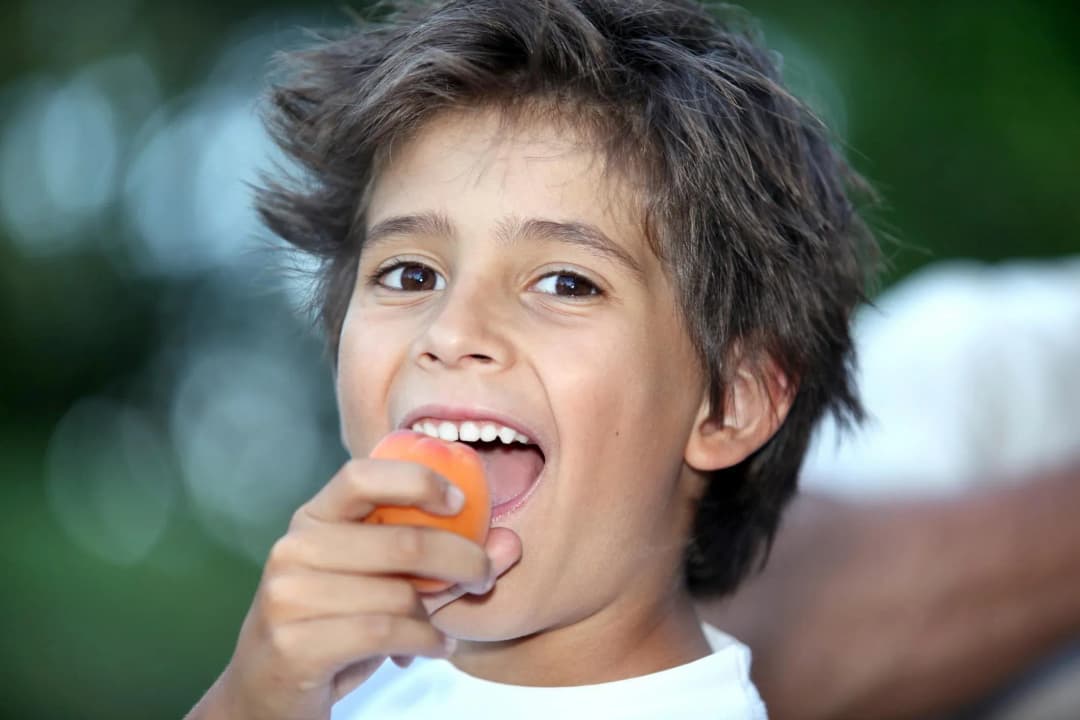 Enfant souriant en tenant un fruit dans sa main avec un fond flou de verdure