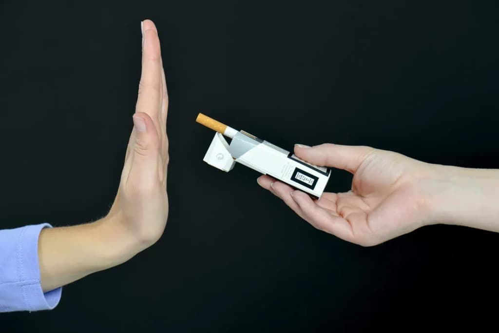 main dans une position de refus face à une cigarette et un dispositif de sevrage