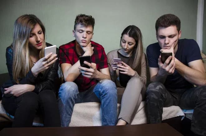 Quatre jeunes absorbés par leurs smartphones assis sur un canapé dans un intérieur.