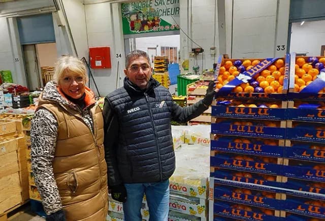 deux personnes souriantes posent devant des caisses d'agrumes dans un entrepôt