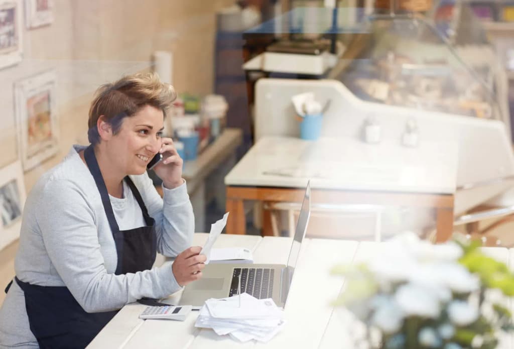 femme souriante au téléphone avec un ordinateur portable et des documents sur une table