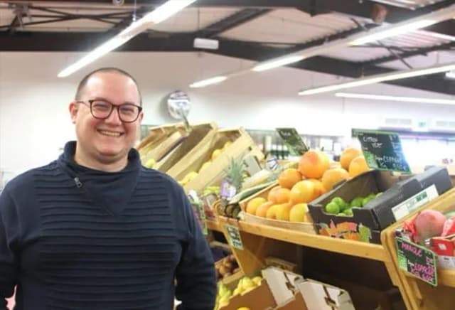 Homme souriant devant des étagères de fruits dans un commerce bio