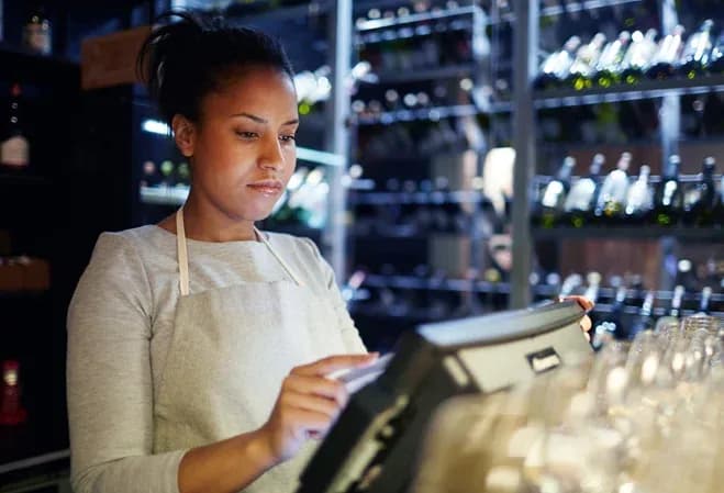 femme en train d'utiliser une caisse enregistreuse dans un bar avec des bouteilles en arrière-plan