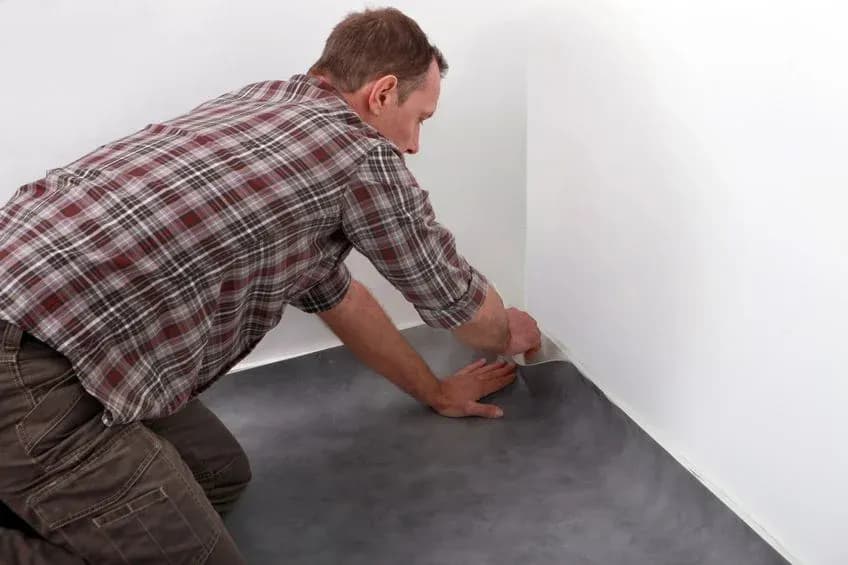 Homme posant un revêtement de sol dans un coin de pièce en se penchant en avant